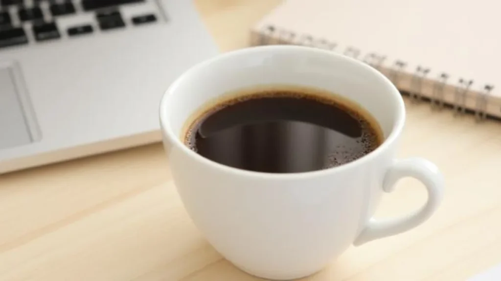 A perfectly brewed cup of black coffee in a white mug on a wooden table beside a small notebook in a bright morning kitchen
