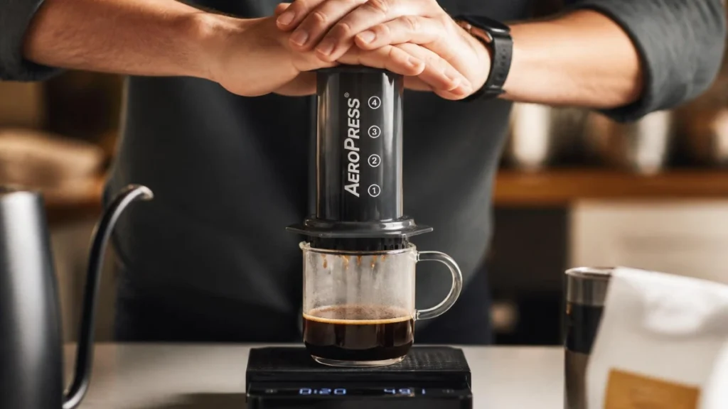 an AeroPress plunger slowly and steadily over a glass mug on a digital scale, coffee dripping into the mug